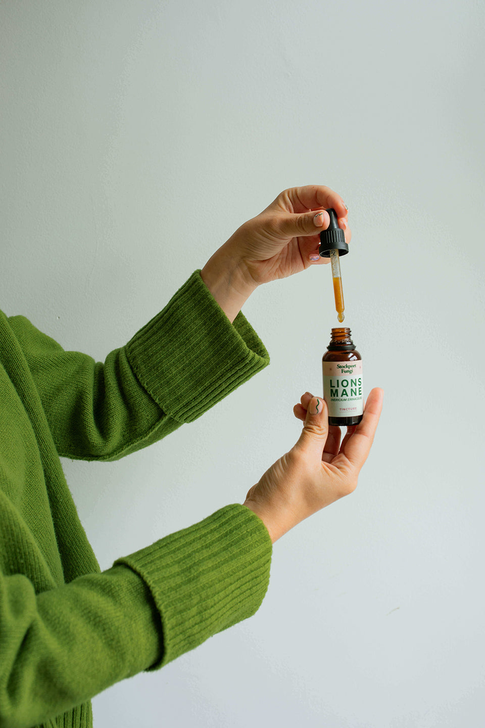 A pair of hands holding a bottle of lions mane tincture with the lid off and the dropper full of liquid